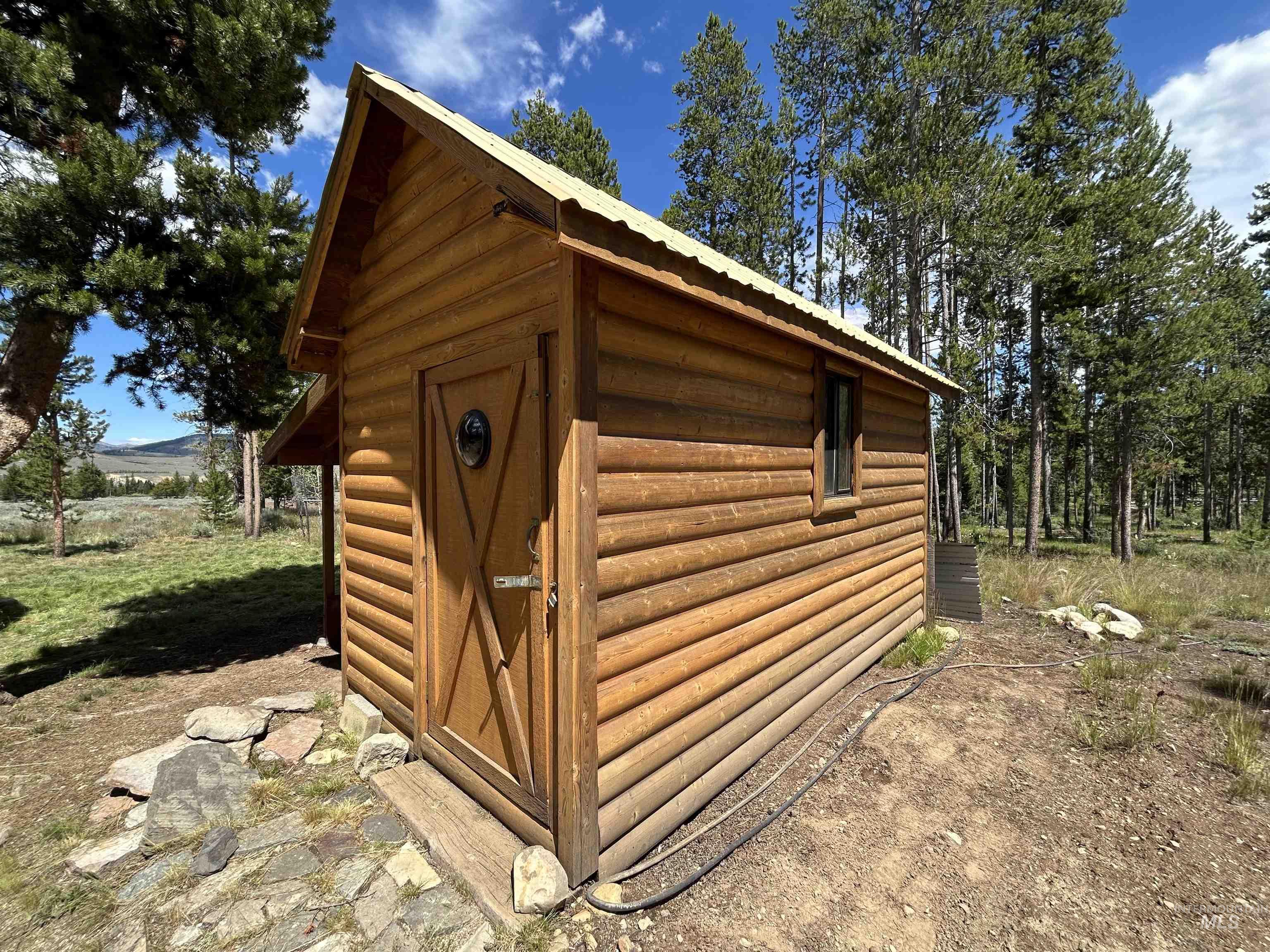 35 Sawtooth Way Stanley, ID 83278 - Photo 28 of 36 Wood-sided structure featuring a gabled roof with metal sheeting, a single window, and a door with a porthole detail