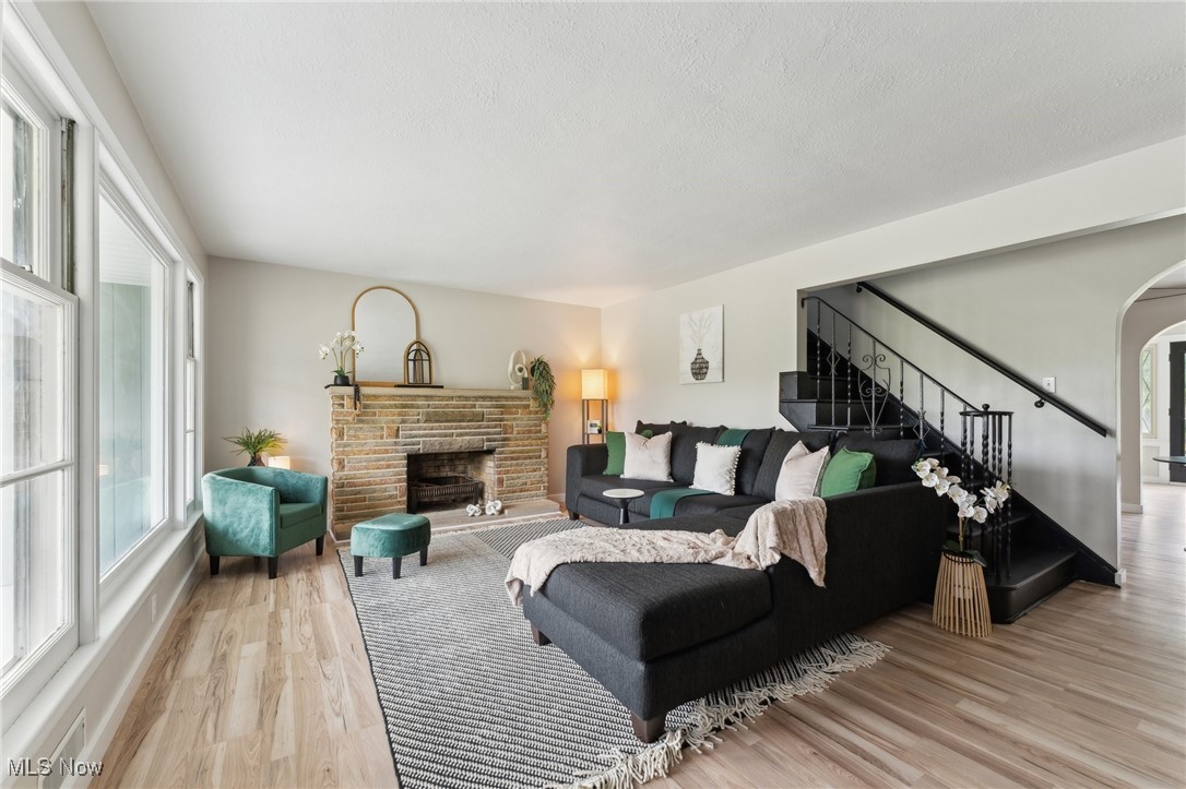 Living area with stairway, wood finished floors, arched walkways, a fireplace, and a textured ceiling