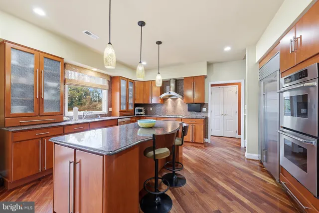 a kitchen with stainless steel appliances granite countertop a kitchen island a stove a refrigerator a oven a dining table and chairs with wooden floor