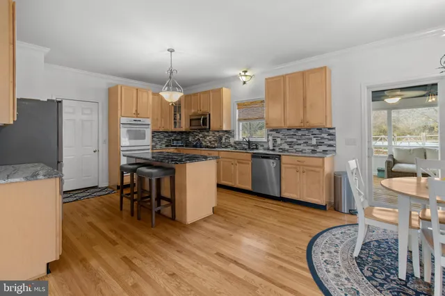 a kitchen with stainless steel appliances granite countertop a stove top oven a sink dishwasher a dining table and chairs with wooden floor