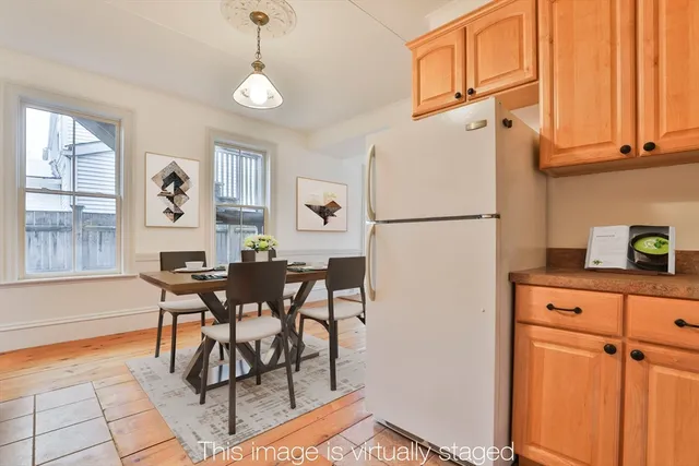 a white kitchen with a refrigerator a stove a dining table and chairs with wooden floor