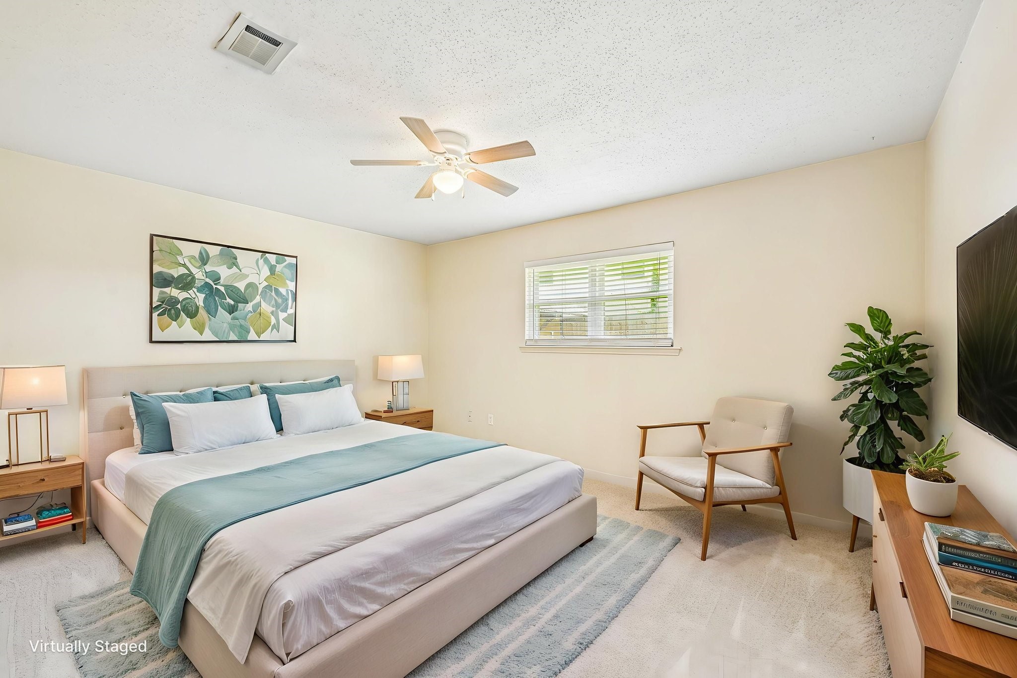 8 Arlington Street Conroe, TX 77301 - Photo 4 of 37 Primary bedroom located downstairs is bright and inviting, featuring a comfortable bed with soft bedding, a ceiling fan, and ample natural light from a window. The room includes stylish furniture, such as nightstands, a chair, and a dresser, with tasteful decor like artwork and plants. The neutral color palette creates a calming atmosphere.