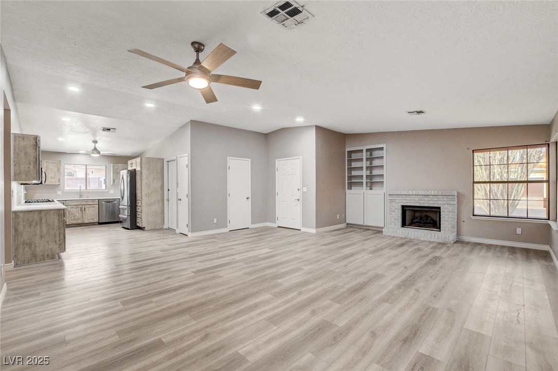 1118 Olmo Way Boulder City, NV 89005 - Photo 3 of 45 Unfurnished living room featuring light wood-style flooring, a brick fireplace, a ceiling fan, recessed lighting, and a textured ceiling