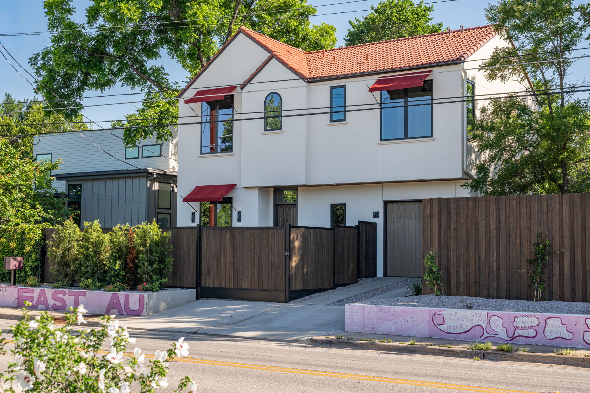 4713 Bolm Road Austin, TX 78702 - Photo 2 of 40 Contemporary stucco facade featuring a red tile roof, red fabric awnings, dark-framed windows, and a private wood fence