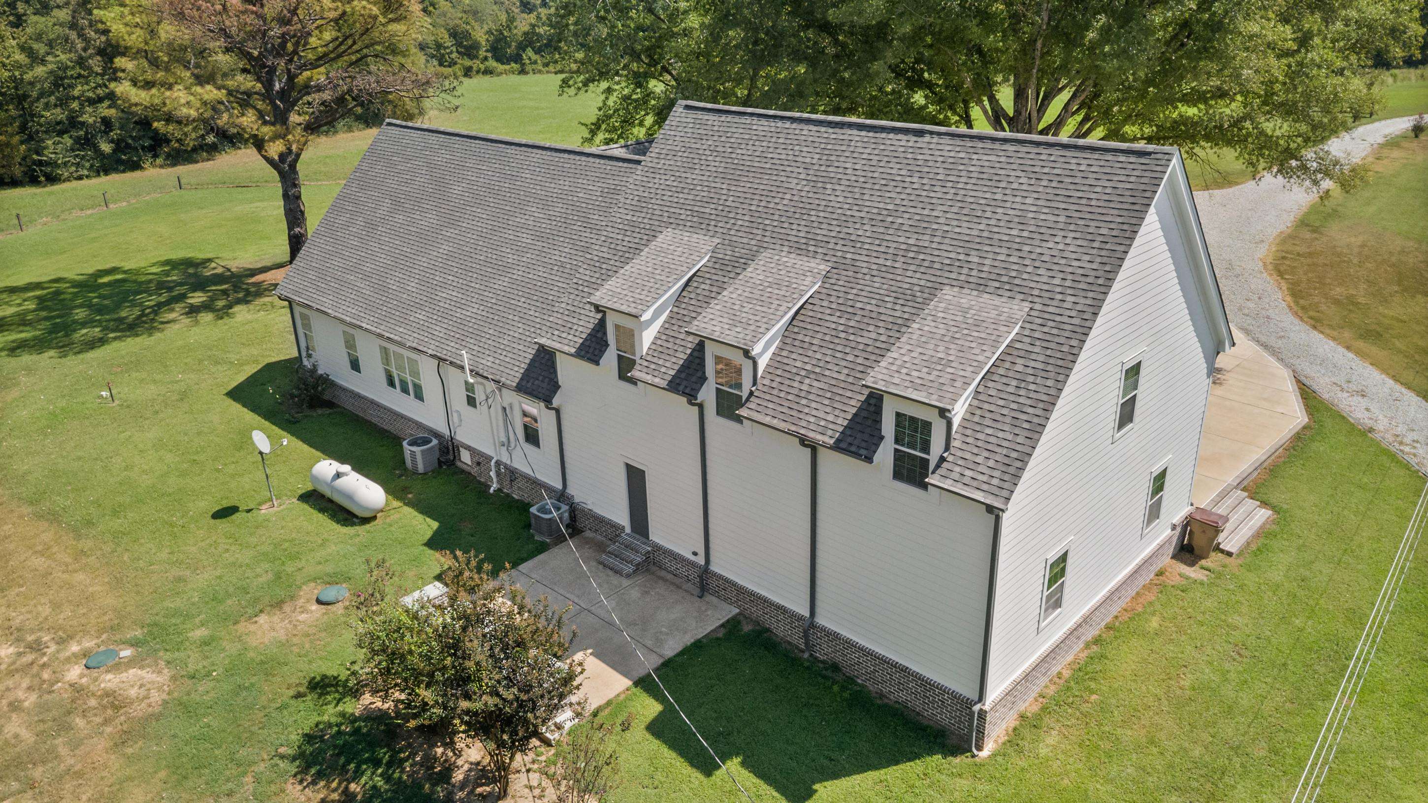 620 Diffee Road Moscow, TN 38057 - Photo 2 of 25 White siding exterior with a dark shingle roof, multiple dormer windows, and a gravel driveway