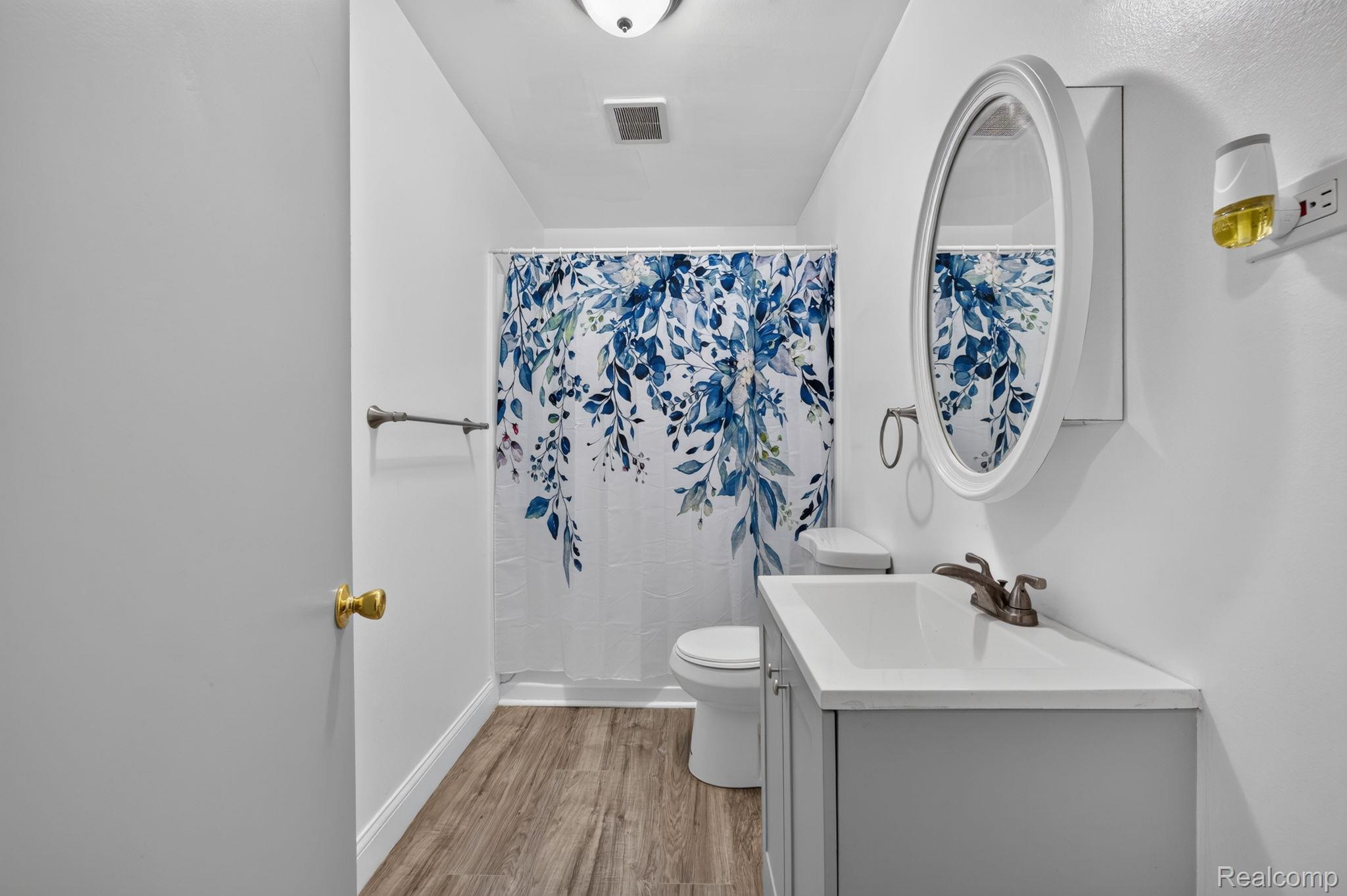9288 Hilda Lane Flushing, MI 48433 - Photo 20 of 50 Bathroom featuring wood-finish flooring, a white vanity with a rectangular sink, an oval wall-mounted mirror, and a toilet