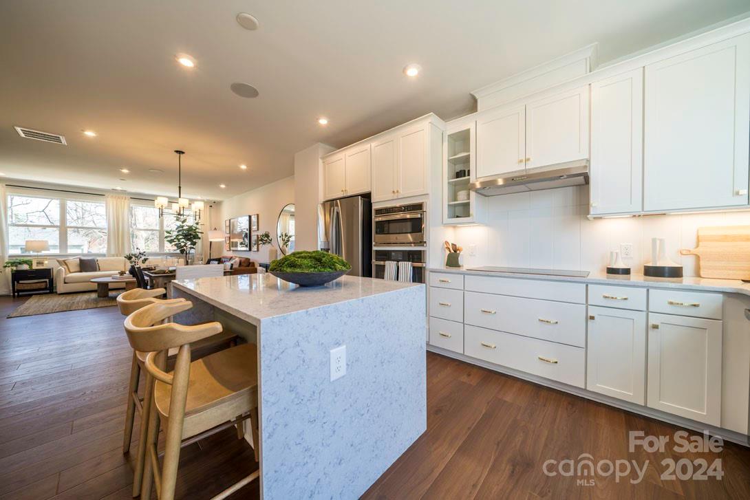 2055 Evolve Way Charlotte, NC 28205 - Photo 2 of 40 a kitchen with stainless steel appliances kitchen island granite countertop a stove a sink a refrigerator and white cabinets with wooden floor