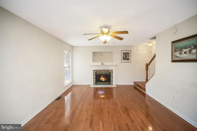 a view of a livingroom with a fireplace a ceiling fan and wooden floor