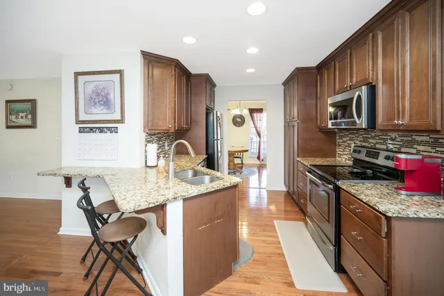 a kitchen with stainless steel appliances granite countertop a stove top oven a sink a refrigerator and chairs