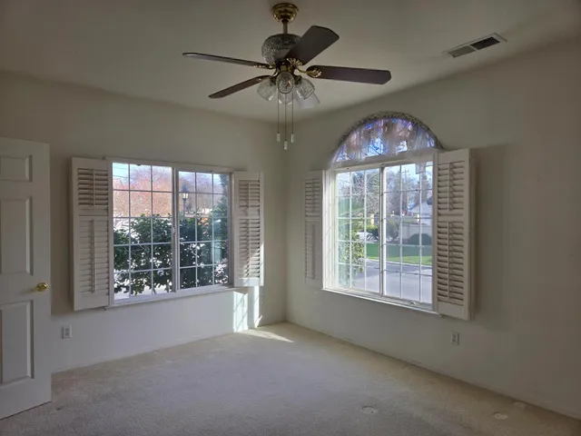 an empty room with chandelier fan and windows