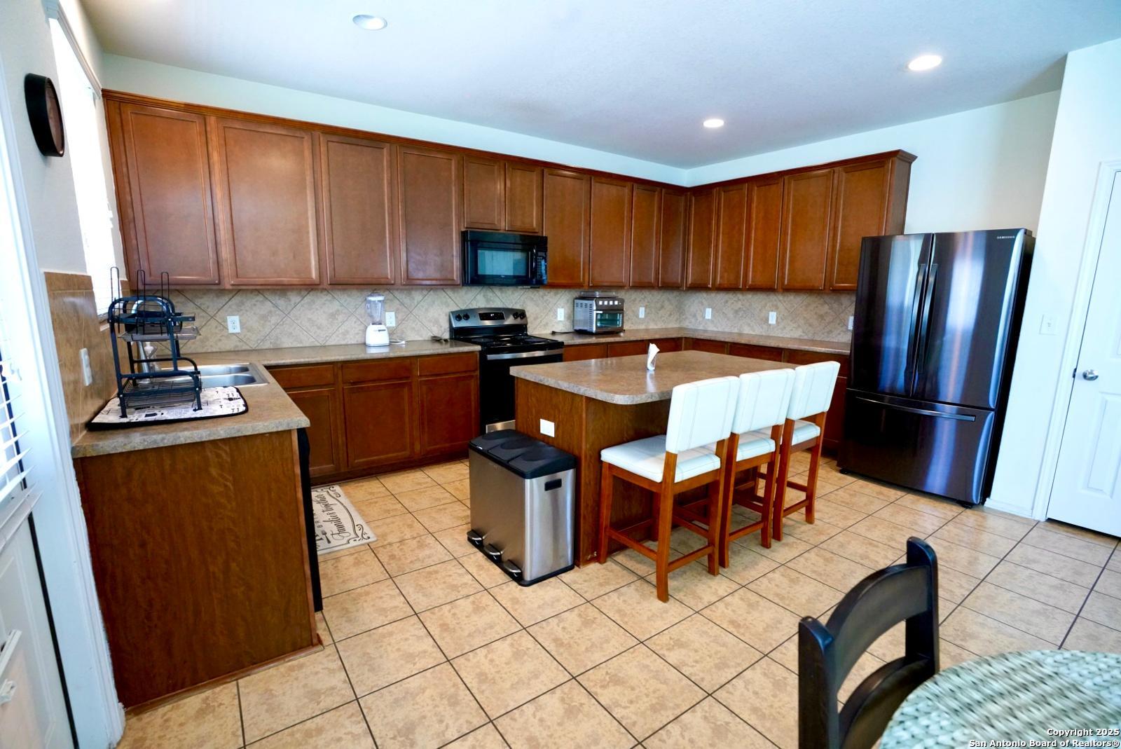 3906 Bent Grass San Antonio, TX 78261 - Photo 9 of 23 a kitchen with stainless steel appliances kitchen island granite countertop a sink a stove a refrigerator a counter top space and cabinets