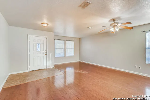 an empty room with chandelier fan and windows