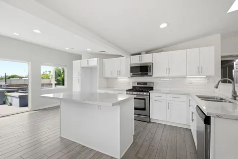 a kitchen with stainless steel appliances granite countertop a sink a stove a refrigerator and white cabinets with wooden floor