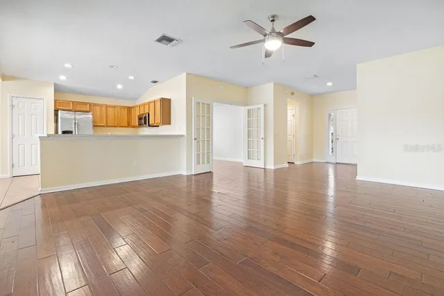 a view of an empty room and kitchen with wooden floor