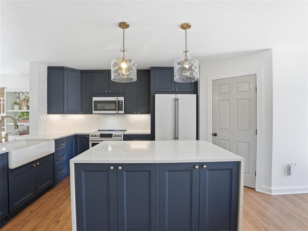 12724 Carpenter Lane Rhome, TX 76078 - Photo 10 of 37 Kitchen featuring a central island with a solid surface countertop, navy shaker cabinetry, stainless steel appliances, a farmhouse sink, and wood-finish flooring