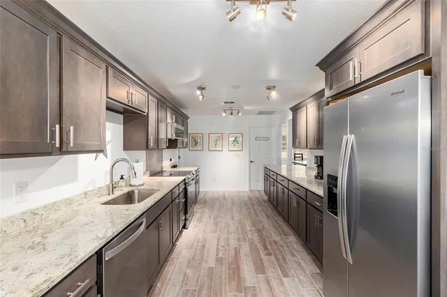 a kitchen with stainless steel appliances granite countertop a refrigerator a sink dishwasher a stove and a wooden cabinets with wooden floor