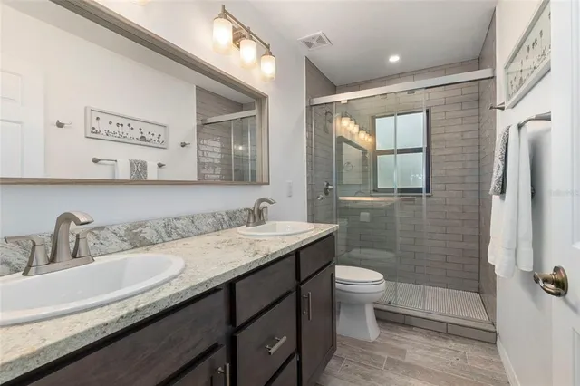 a bathroom with a granite countertop sink a toilet a mirror and shower