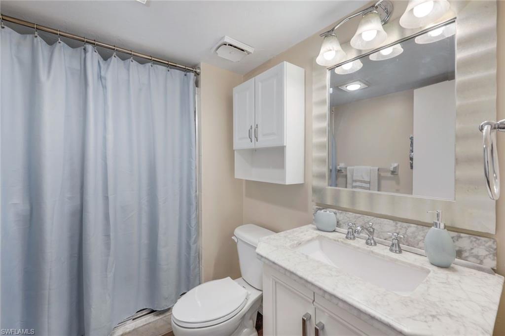 10475 Gulf Shore Drive, Unit 142 Naples, FL 34108 - Photo 13 of 14 a bathroom with a granite countertop sink toilet a mirror a vanity and shower
