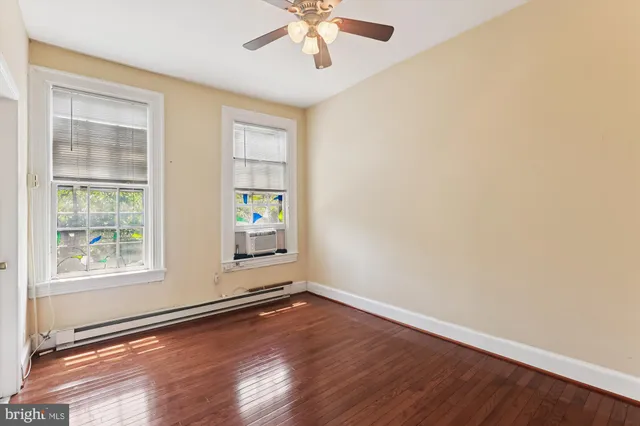 an empty room with wooden floor chandelier fan and windows