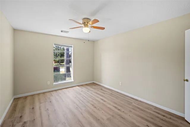 an empty room with wooden floor chandelier fan and windows