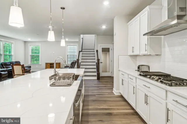 a kitchen with stainless steel appliances kitchen island granite countertop a stove a sink a refrigerator and white cabinets with wooden floor