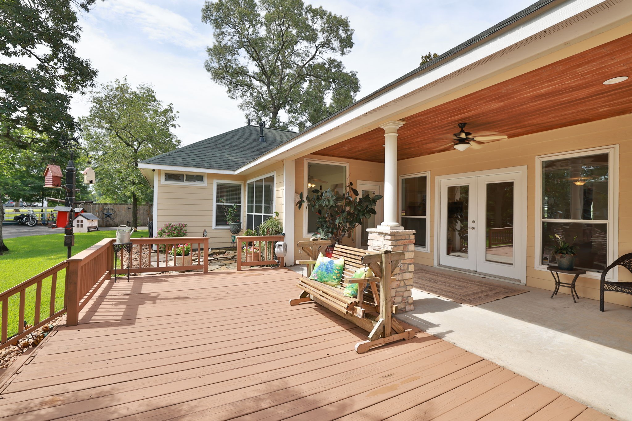 34310 High Point Drive Magnolia, TX 77355 - Photo 23 of 48 This photo showcases a spacious wooden deck with a cozy covered patio area. The patio features ceiling fans, ample seating, and large windows, offering a welcoming outdoor space with a view of the lush backyard.