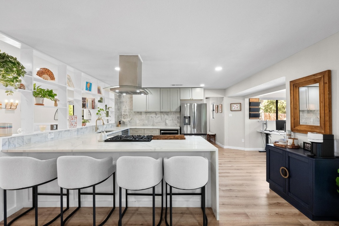 1006 Hollybluff Street Austin, TX 78753 - Photo 8 of 27 Kitchen with light stone countertops, a kitchen bar, open shelves, light wood-type flooring, and a peninsula