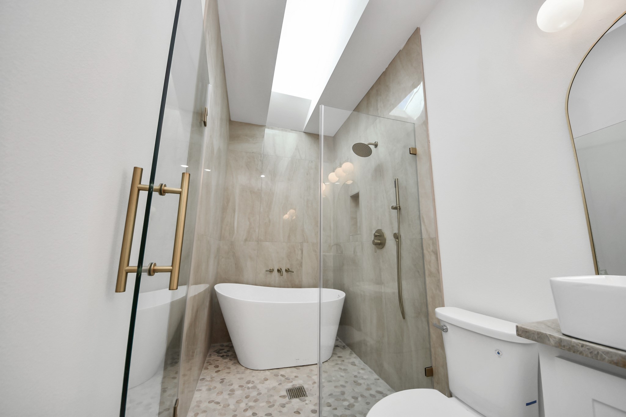 427 North Milby Street Houston, TX 77003 - Photo 17 of 44 Spa-like bathroom retreat featuring a freestanding soaking tub, glass-enclosed shower with designer gold fixtures, and beautiful marble-style tile. Skylight above fills the space with natural light, creating a bright and luxurious feel.