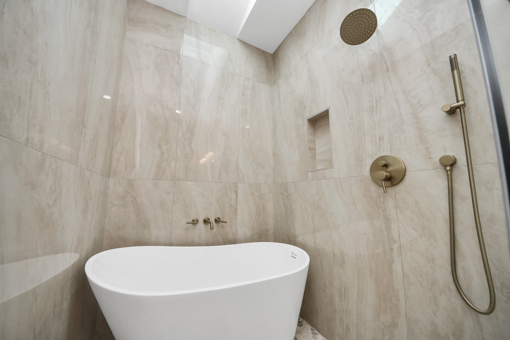427 North Milby Street Houston, TX 77003 - Photo 18 of 44 Spa-like bathroom retreat featuring a freestanding soaking tub, glass-enclosed shower with designer gold fixtures, and beautiful marble-style tile. Skylight above fills the space with natural light, creating a bright and luxurious feel.
