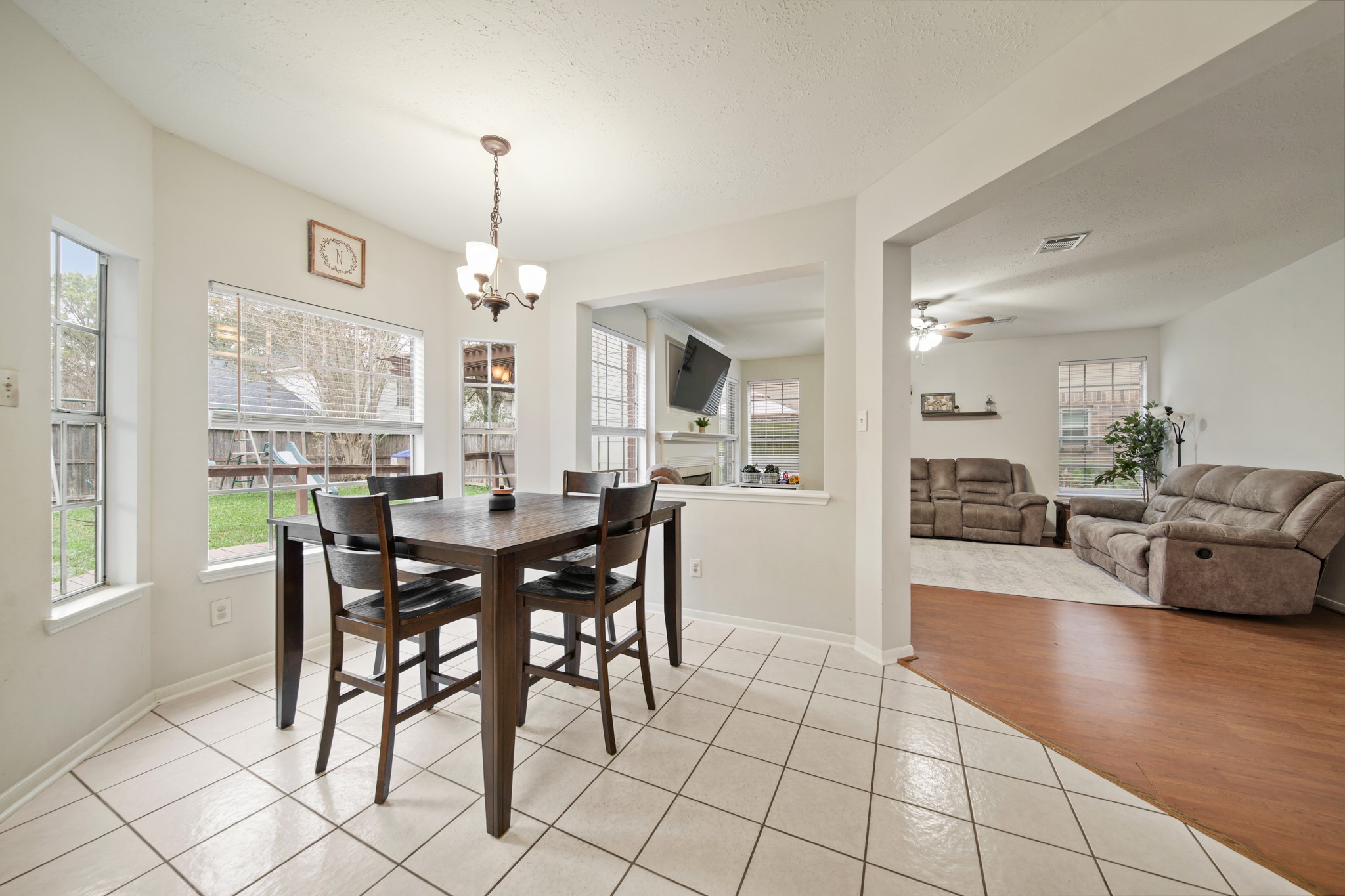 16114 Kintyre Point Road Houston, TX 77095 - Photo 27 of 44 This photo showcases a bright dining area with a dark wood table and chairs, adjacent to a cozy living room with plush seating. Large windows offer ample natural light, and the open layout provides a spacious feel. The tiled floor in the dining area transitions to wood flooring in the living space, creating a warm and inviting atmosphere.