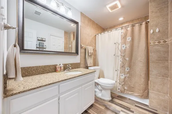 a bathroom with a granite countertop sink a toilet a mirror and shower