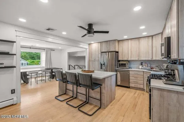 a kitchen with stainless steel appliances kitchen island granite countertop a stove a sink a dining table and chairs with wooden floor