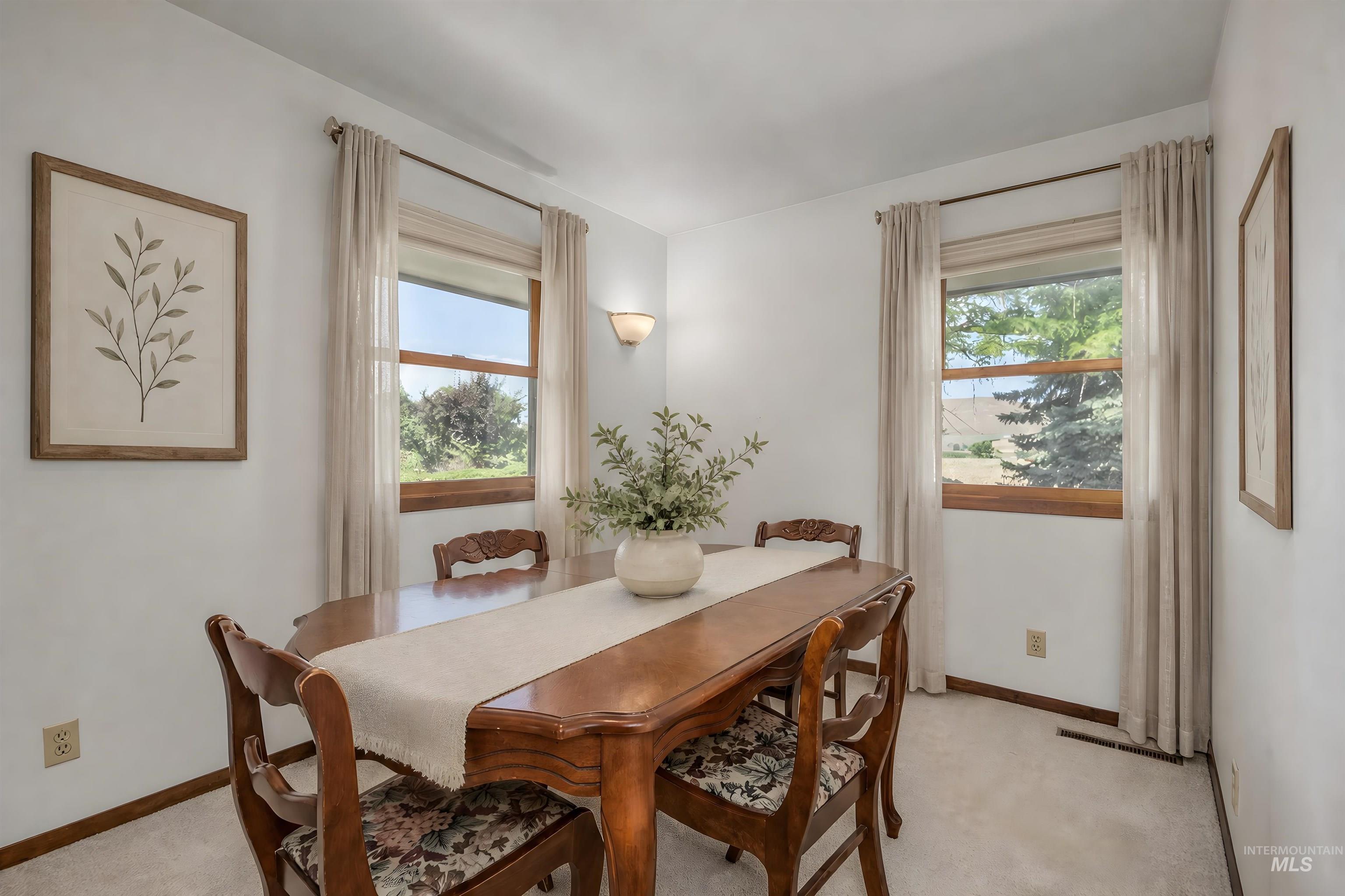 1493 Cove Road Weiser, ID 83672 - Photo 8 of 50 Carpeted room with a wooden dining table, a pair of windows with wooden frames and light-colored curtains, and a wall sconce