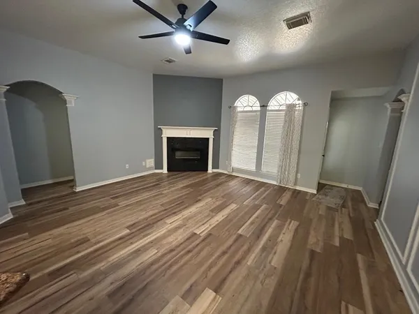 an empty room with wooden floor fan and windows