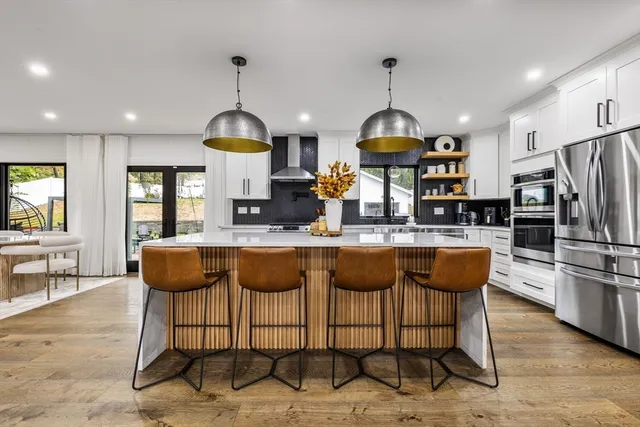 a kitchen with stainless steel appliances kitchen island granite countertop a refrigerator a stove a dining table and chairs with wooden floor