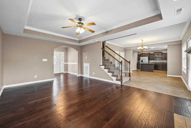 a view of an empty room with wooden floor and a ceiling fan