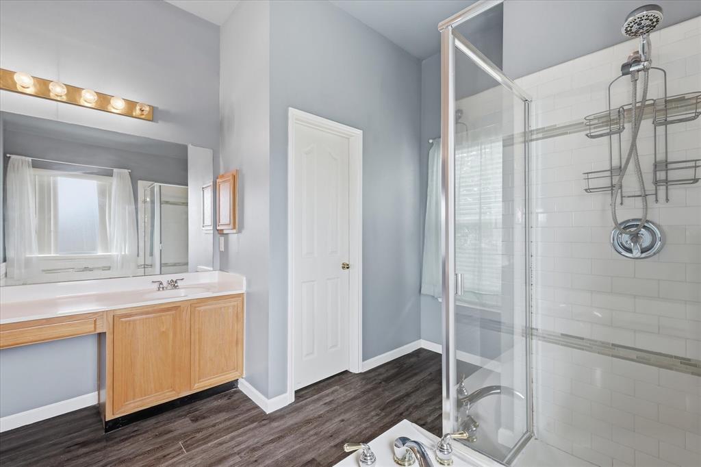 4545 Ridgepointe Drive The Colony, TX 75056 - Photo 27 of 37 Bathroom featuring a glass-enclosed shower with subway tile surround, a light wood-finish vanity with an integrated sink, a large wall mirror, and wood-finish flooring
