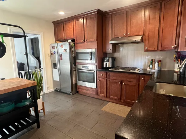 a kitchen with stainless steel appliances granite countertop a refrigerator a stove and a sink with wooden cabinets