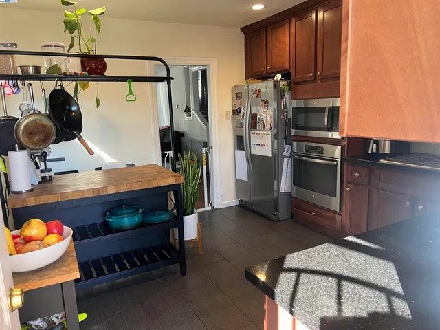 a kitchen with stainless steel appliances kitchen island granite countertop a refrigerator a stove and a sink with wooden floor