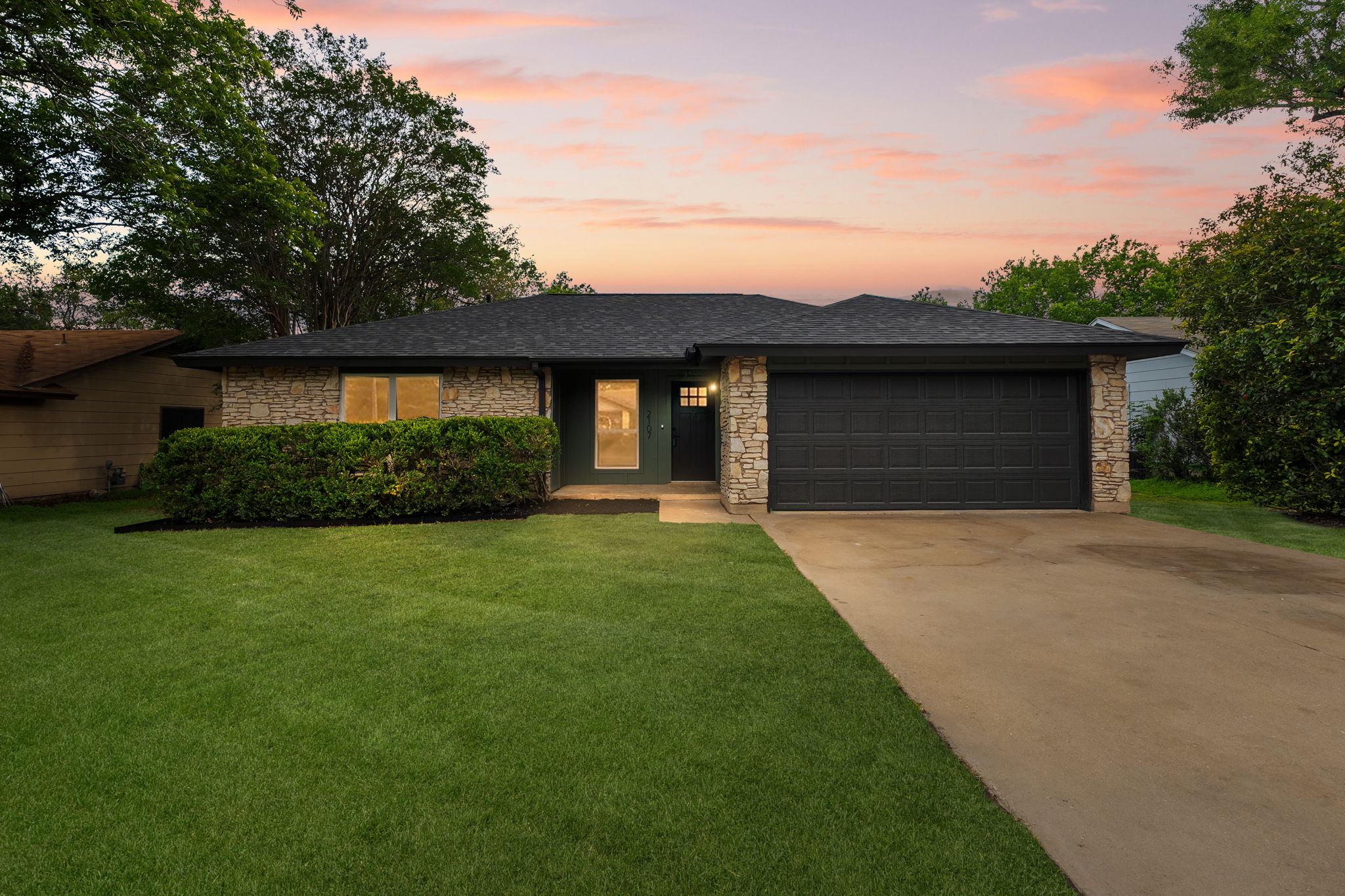 2107 Cindy Lane Austin, TX 78727 - Photo 1 of 33 Single-story residence featuring a stone and siding exterior, an attached garage with a dark paneled door, a dark shingle roof, and a concrete driveway