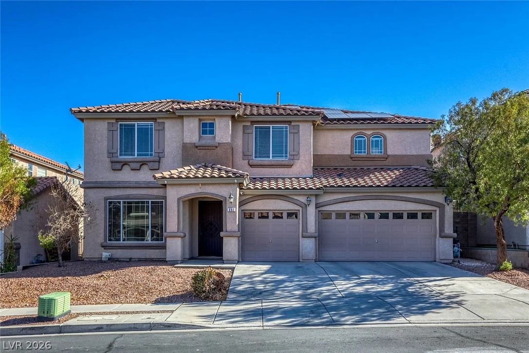 Mediterranean / spanish-style home with roof mounted solar panels, stucco siding, driveway, and an attached garage