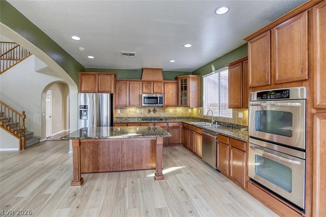692 Blue Crystal Creek Road Henderson, NV 89002 - Photo 11 of 29 Kitchen featuring stainless steel appliances, wood finish cabinets, dark stone countertops, light wood finished floors, and arched walkways