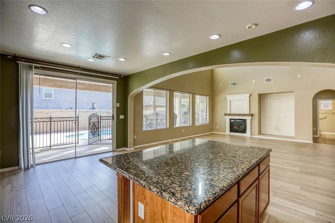 692 Blue Crystal Creek Road Henderson, NV 89002 - Photo 13 of 29 Kitchen featuring dark stone counters, arched walkways, light wood-style floors, a textured ceiling, and a center island