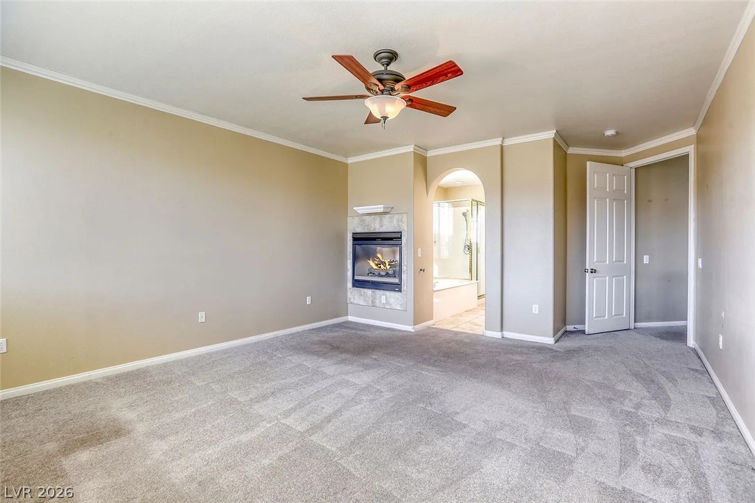 692 Blue Crystal Creek Road Henderson, NV 89002 - Photo 18 of 29 Unfurnished living room featuring a tiled fireplace, a ceiling fan, crown molding, light carpet, and arched walkways