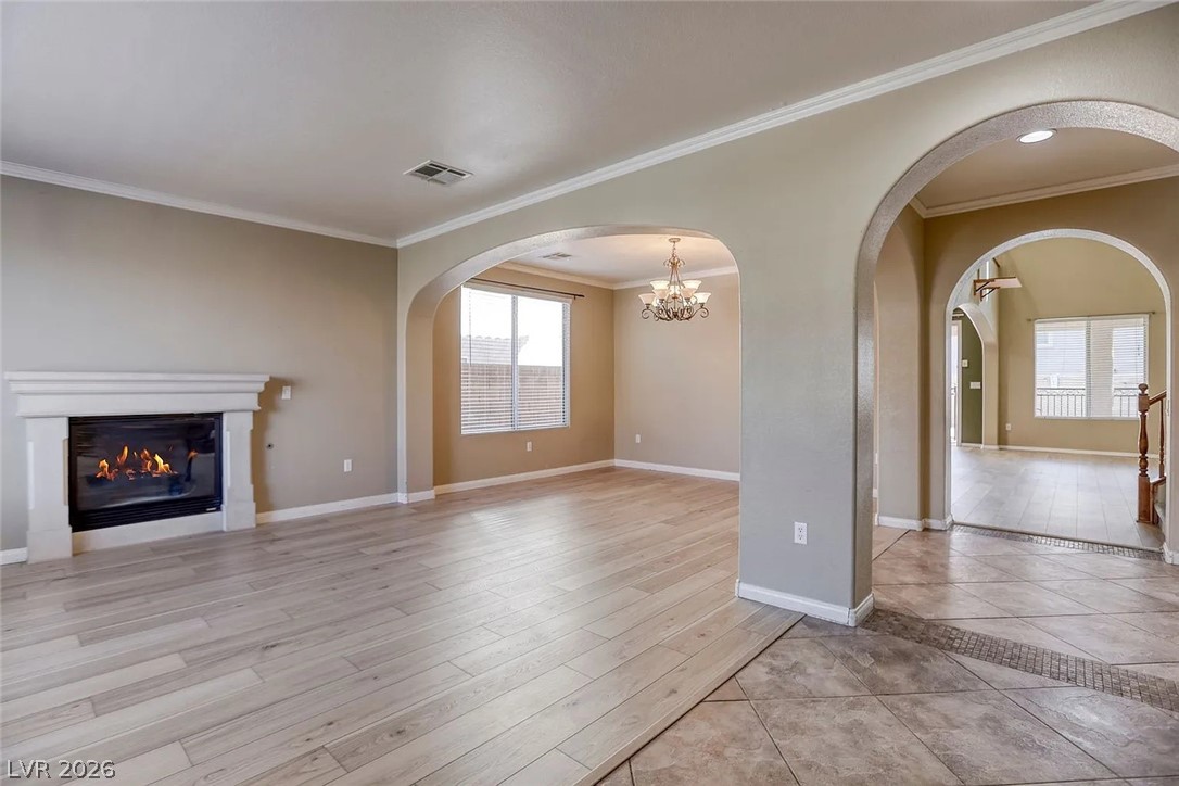 692 Blue Crystal Creek Road Henderson, NV 89002 - Photo 28 of 29 Unfurnished living room featuring ornamental molding, a glass covered fireplace, light wood-style flooring, and a chandelier
