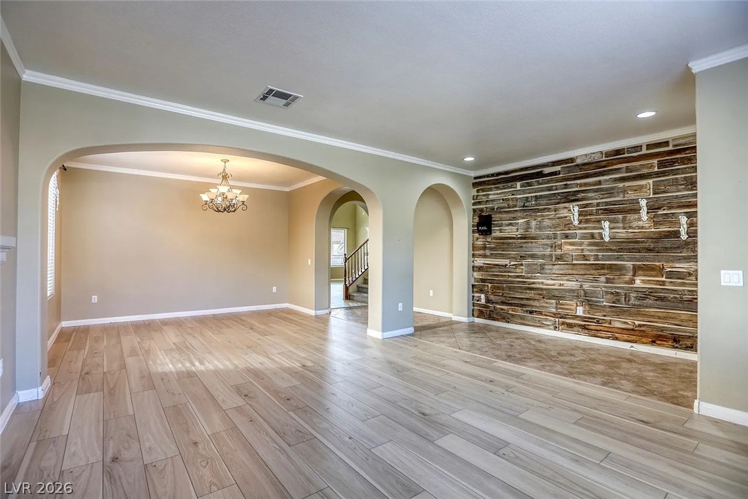 692 Blue Crystal Creek Road Henderson, NV 89002 - Photo 9 of 29 Unfurnished living room with an accent wall, wood walls, crown molding, light wood-style floors, and a chandelier