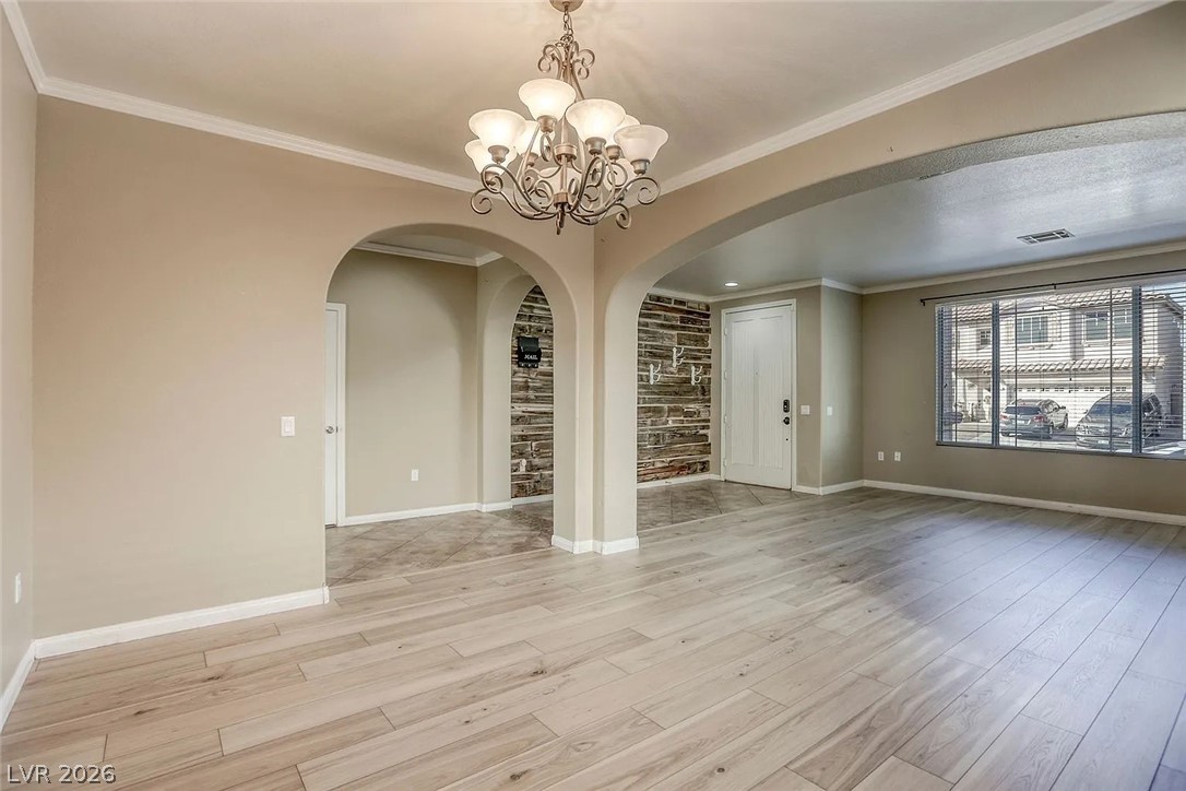 692 Blue Crystal Creek Road Henderson, NV 89002 - Photo 10 of 29 Spare room featuring a chandelier, ornamental molding, light wood-style floors, and arched walkways