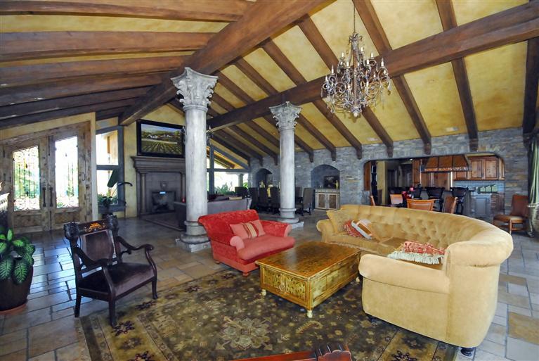 4678 Millerton Road Friant, CA 93626 - Photo 12 of 86 The Great Room ~ Wood, glass & iron double Entry doors open to reveal this Grand Room with vaulted beam ceiling, stone flooring, large Corinthian columns, stacked stone wall with built-in stone arches and temperature controlled wine vault. This room is host to two sitting areas (one with a stone fireplace the other with a built-in custom designed bookshelf/hutch), Dining Area and Breakfast Area.
