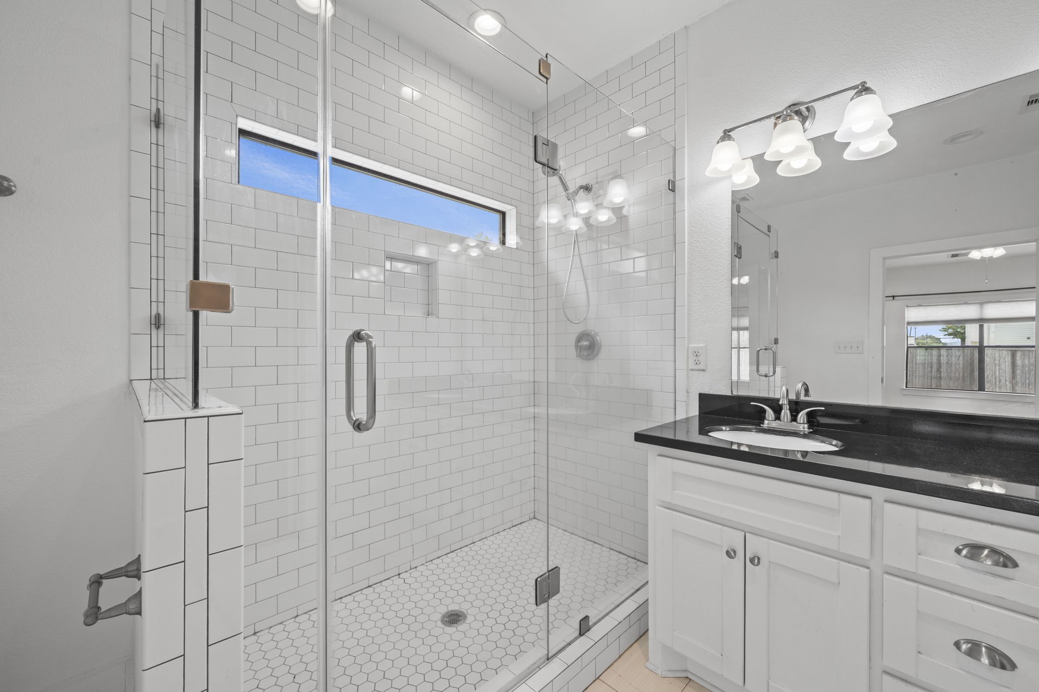 4734 Bell Street, Unit B Houston, TX 77023 - Photo 7 of 10 Updated bathroom with glass-enclosed shower, subway tile surround, hex tile shower floor, black countertop vanity, and bright lighting.