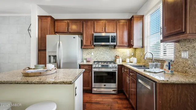a kitchen with granite countertop kitchen island stainless steel appliances a sink a stove a refrigerator cabinets and a window